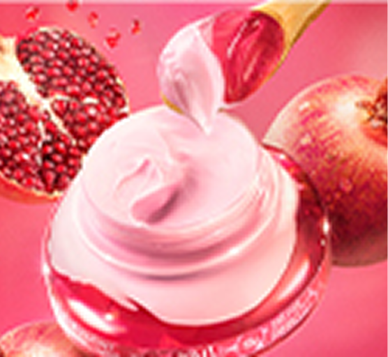 A imagem mostra um frasco de creme com um tom rosado, com uma colher de madeira retirando o produto, ao lado de romãs ao fundo. O cenário é vibrante, com uma tonalidade de rosa predominante, criando um visual suave e delicado.