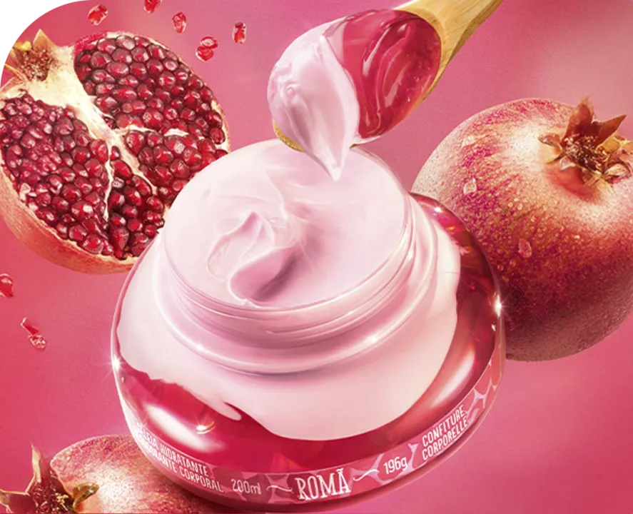 A imagem mostra um frasco de creme com um tom rosado, com uma colher de madeira retirando o produto, ao lado de romãs ao fundo. O cenário é vibrante, com uma tonalidade de rosa predominante, criando um visual suave e delicado.
