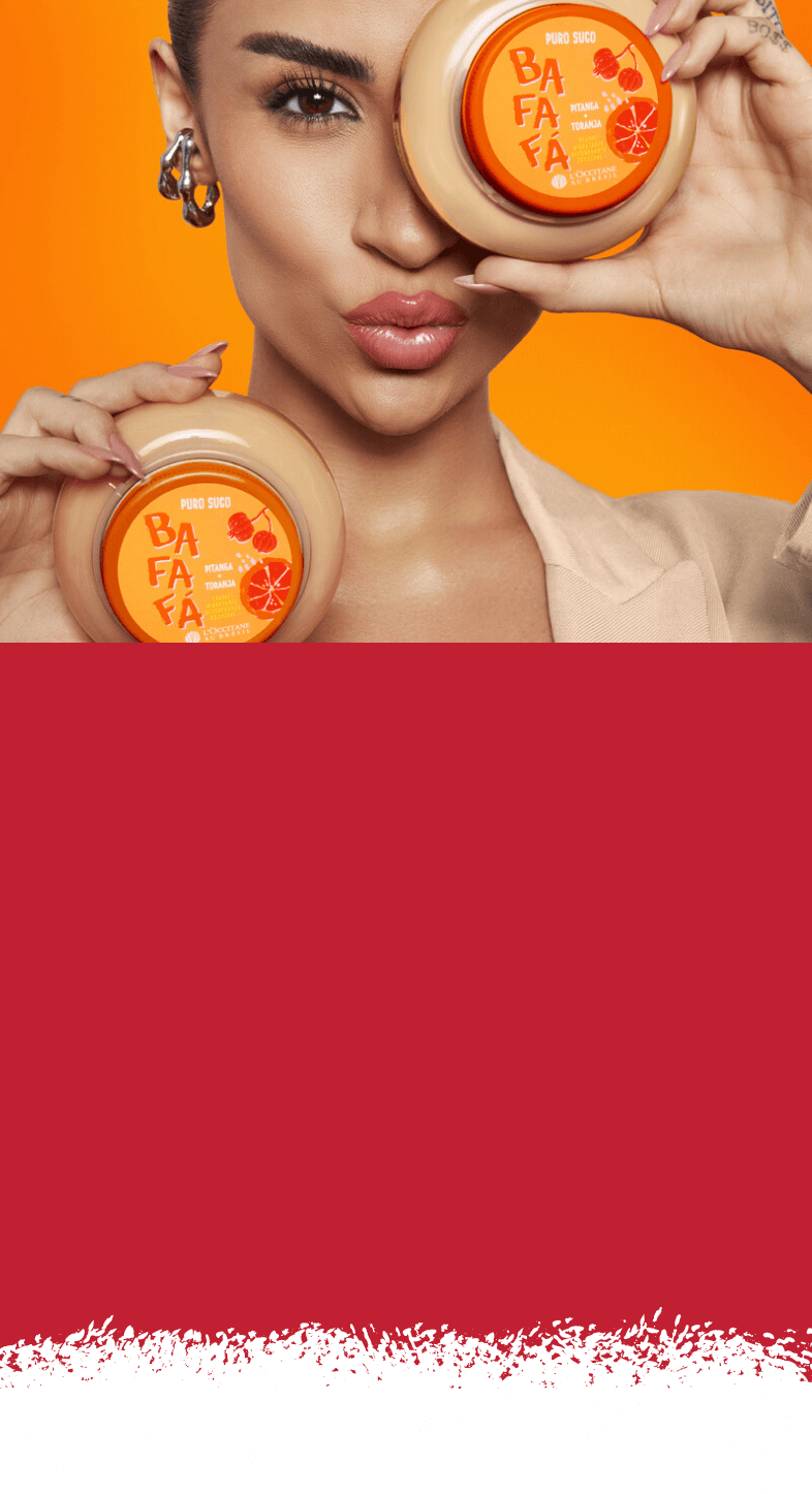 Mulher segurando dois frascos de produtos cosméticos nas mãos, com roupa salmão e com parede laranja ao fundo e ambiente em tons quentes